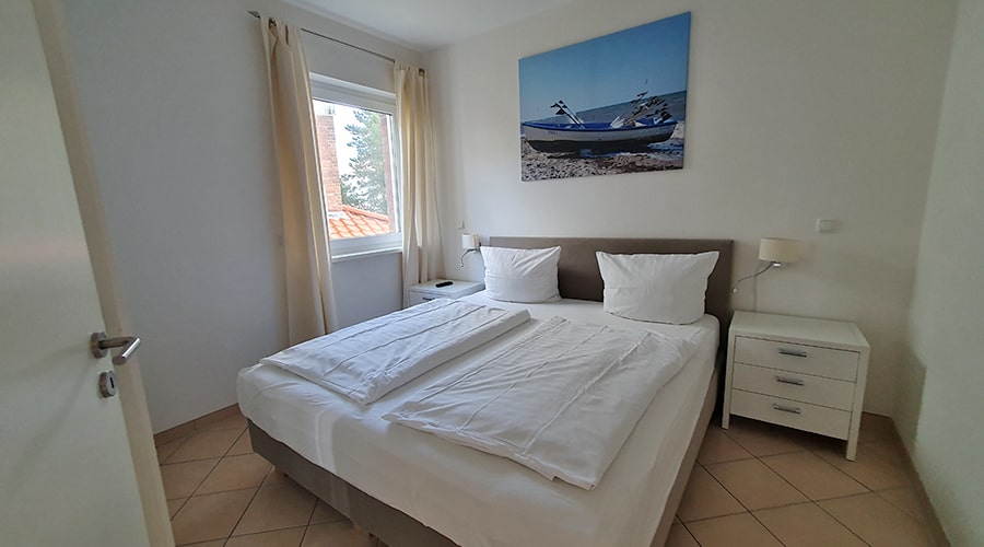 Schlafzimmer mit weißer Bettwäsche und Wandbild einer gelben Feldlandschaft unter blauem Himmel